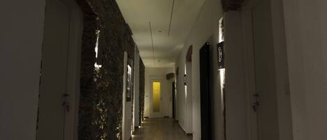 A hallway with stone walls, wooden flooring, and doors on both sides.