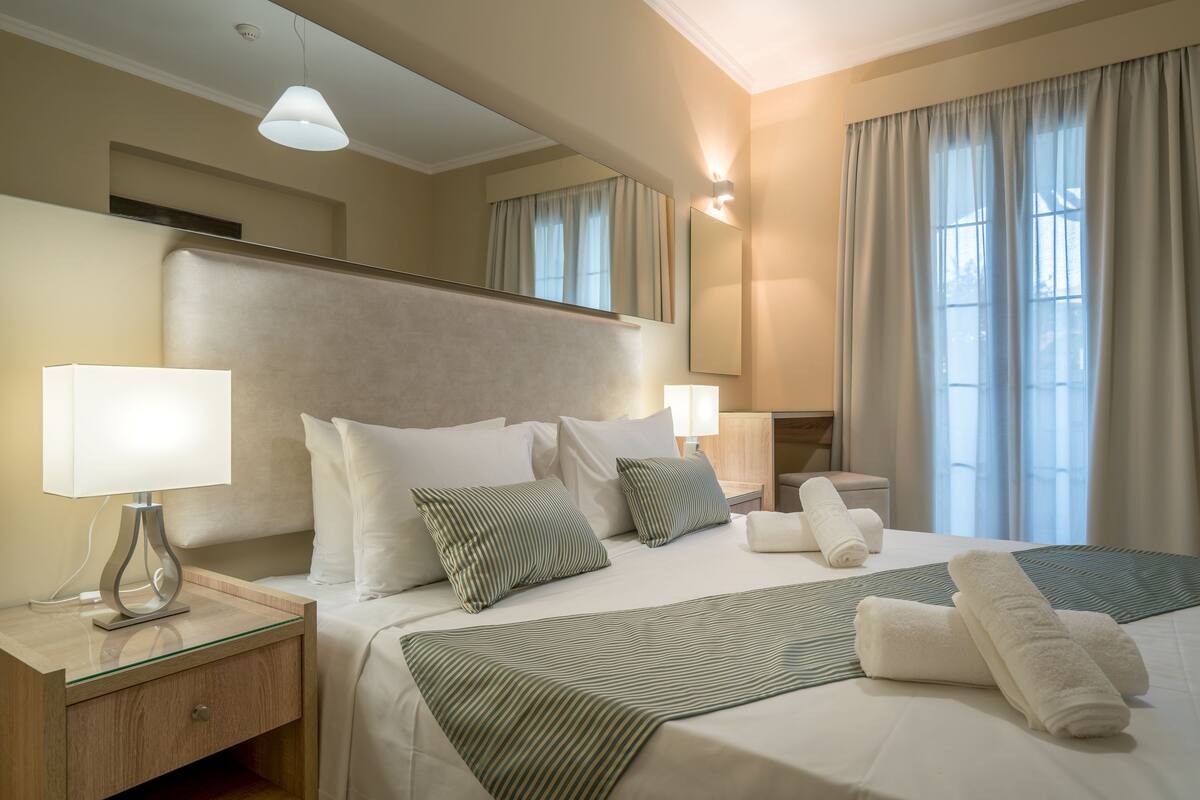 A hotel room with a large bed, two bedside tables, a mirror, and a window with curtains.