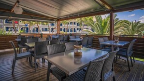 An outdoor patio with tables and chairs, overlooking a building with blue windows and balconies. - Golden Sun Hotel (Zakynthos)