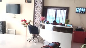 A reception area with a reception desk, a TV, a large window, and a seating area with massage chairs. - Hotel The Royal Buddha (Gaya)