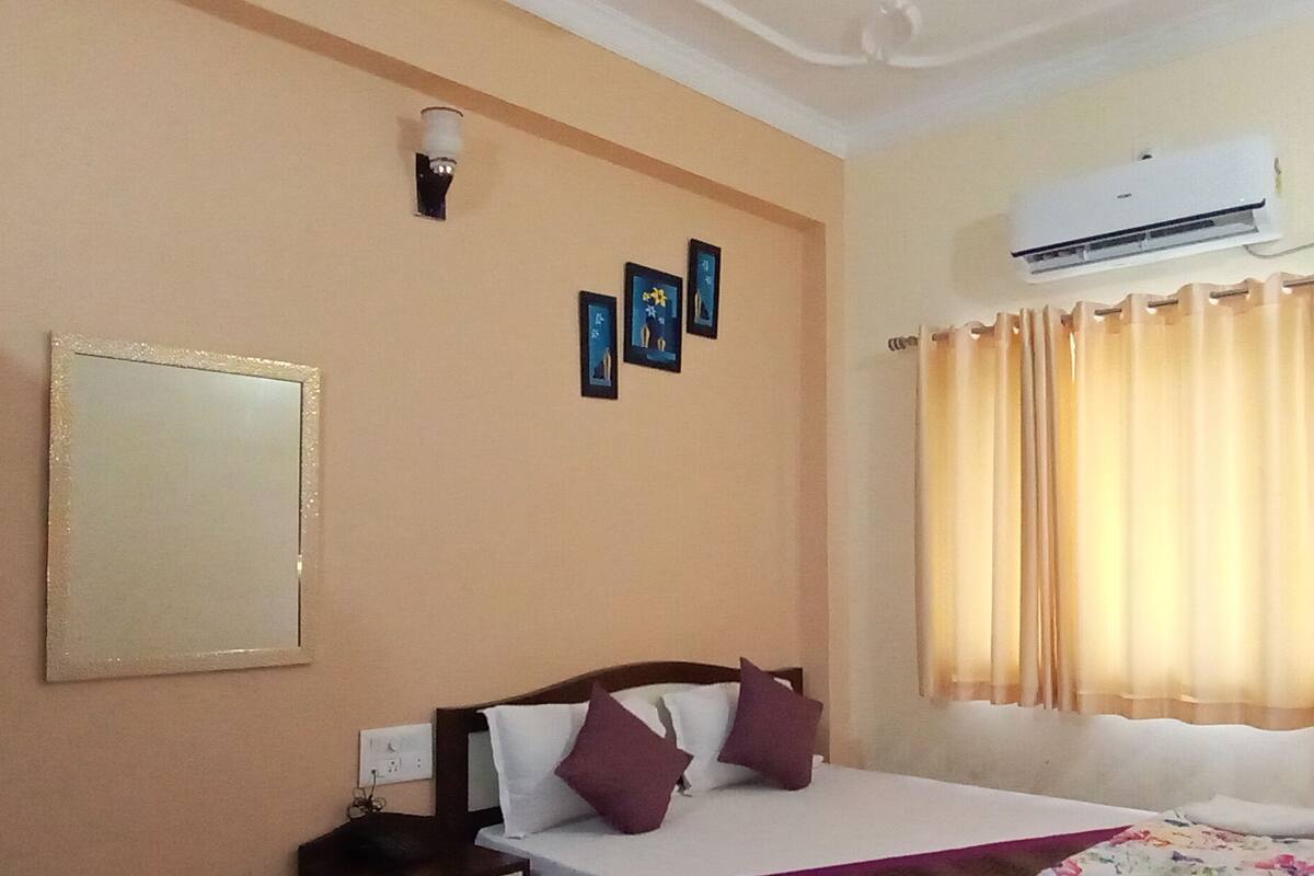 Une chambre à coucher comprenant un lit, un climatiseur fixé au mur, une fenêtre avec des rideaux et un luminaire fixé au mur.