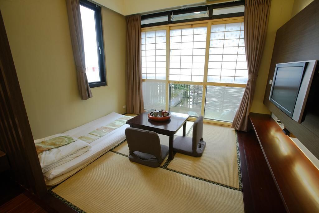 A room with tatami flooring, a low table with cushions, a TV, and a large window with curtains.