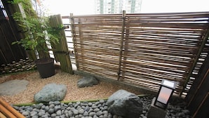 Un jardí zen amb tanca de bambú, roques i una planta en test.