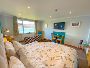 Un dormitorio con una cama grande, un escritorio, una silla, una ventana con vista al mar y un cuadro en la pared.