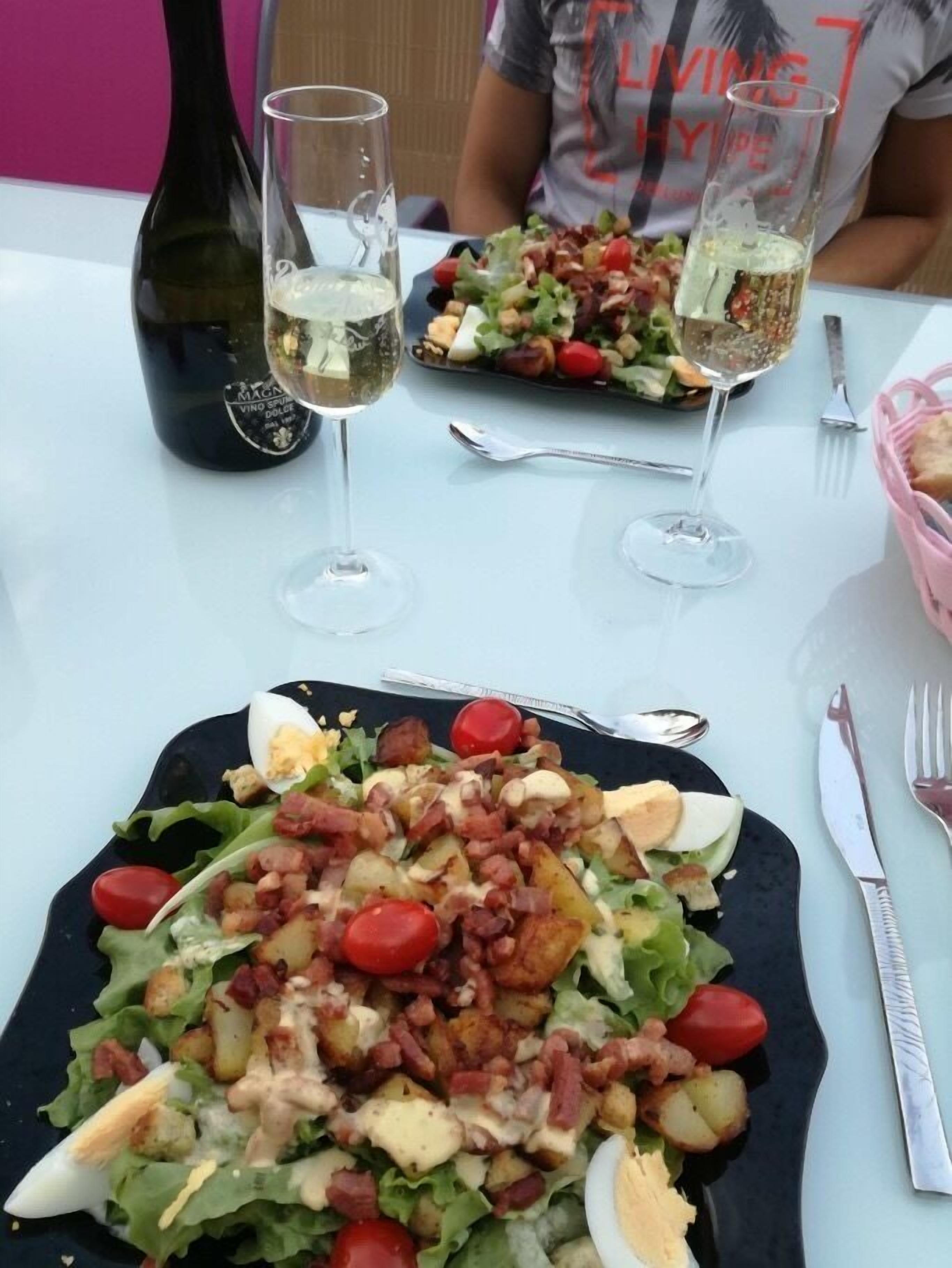 A dining table with a salad, two wine glasses, and a bottle of wine.
