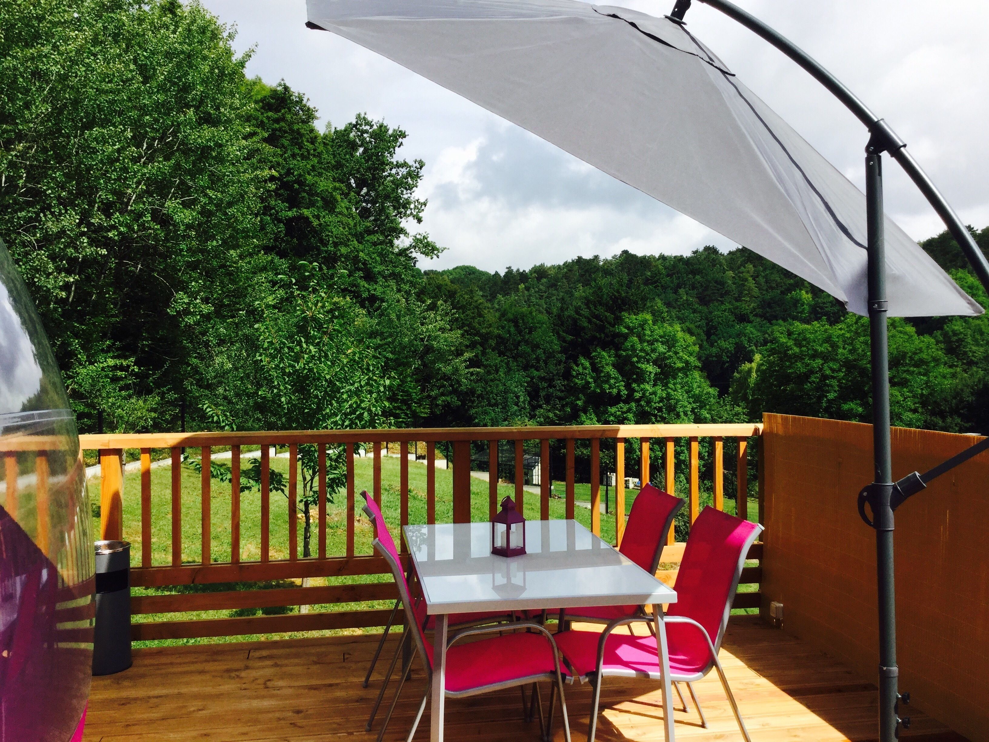 A wooden deck with a table and chairs, a grill, and a white umbrella.