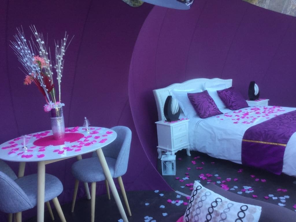 A bedroom with a bed, nightstands, a bedside table, a chair, and a small table with a vase of flowers.