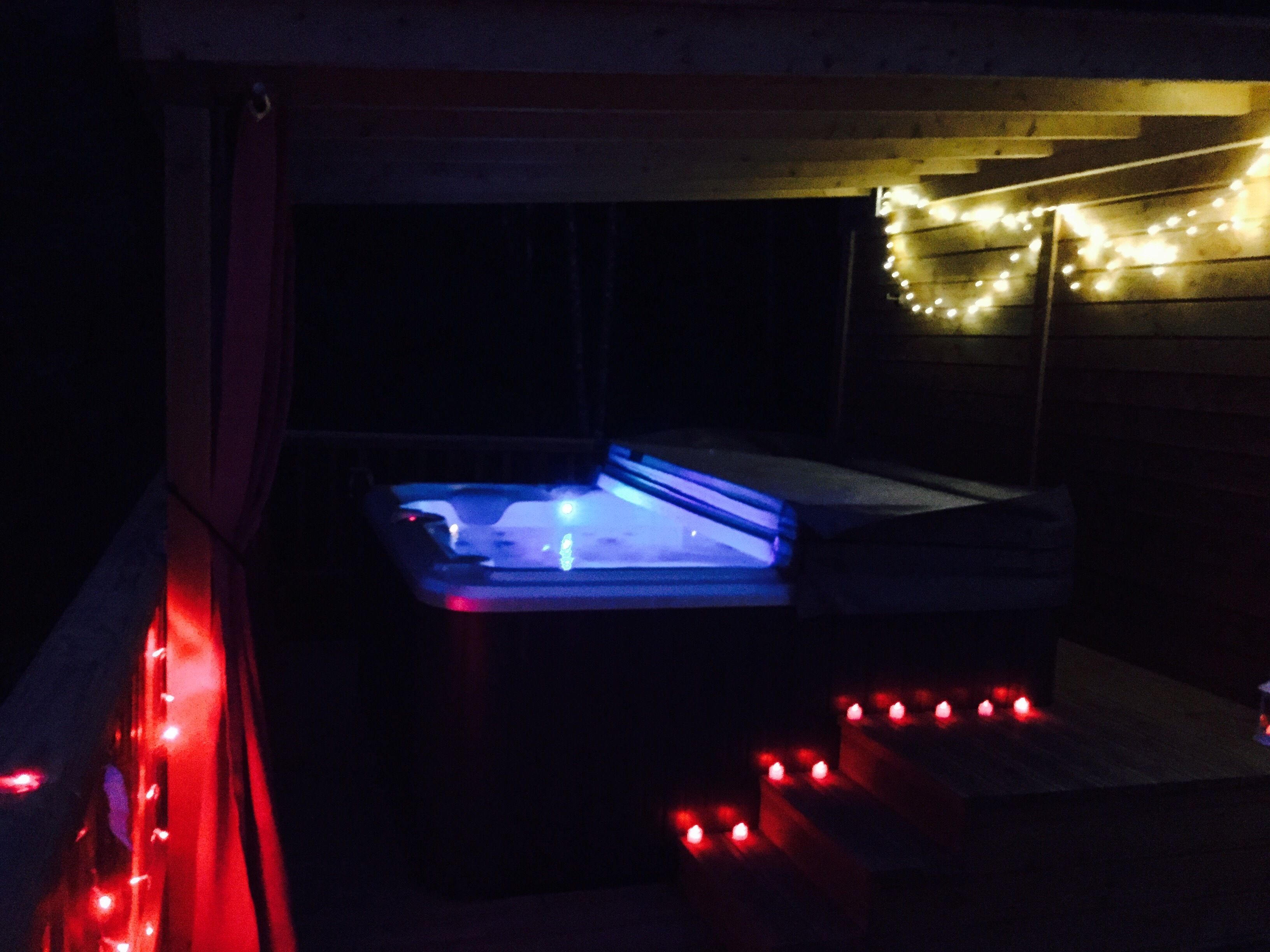 A hot tub with blue lighting, surrounded by red lights, and a string of lights above.