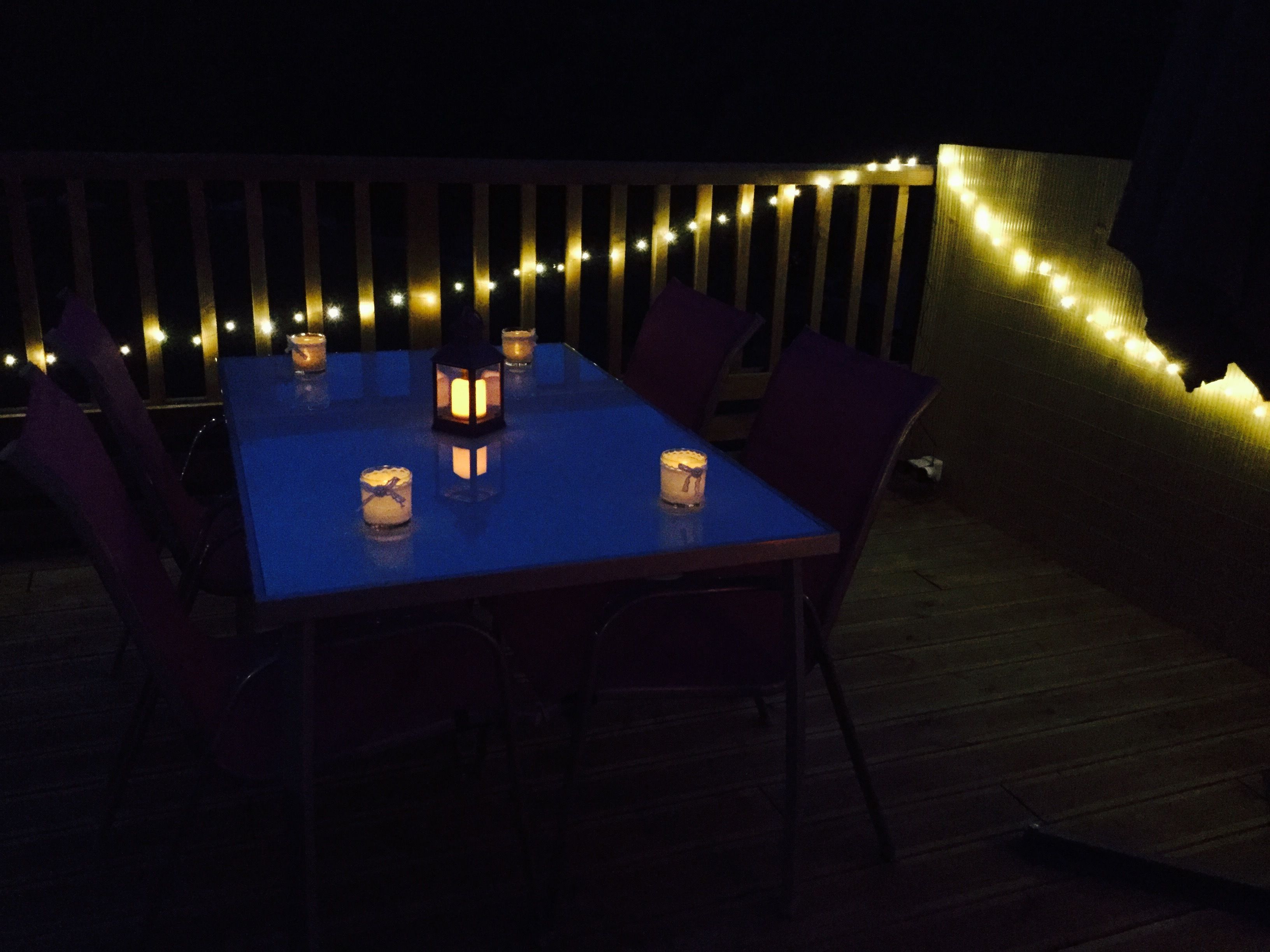 Un espace de restauration en plein air, avec une table et des chaises, éclairé par des bougies et des guirlandes lumineuses.