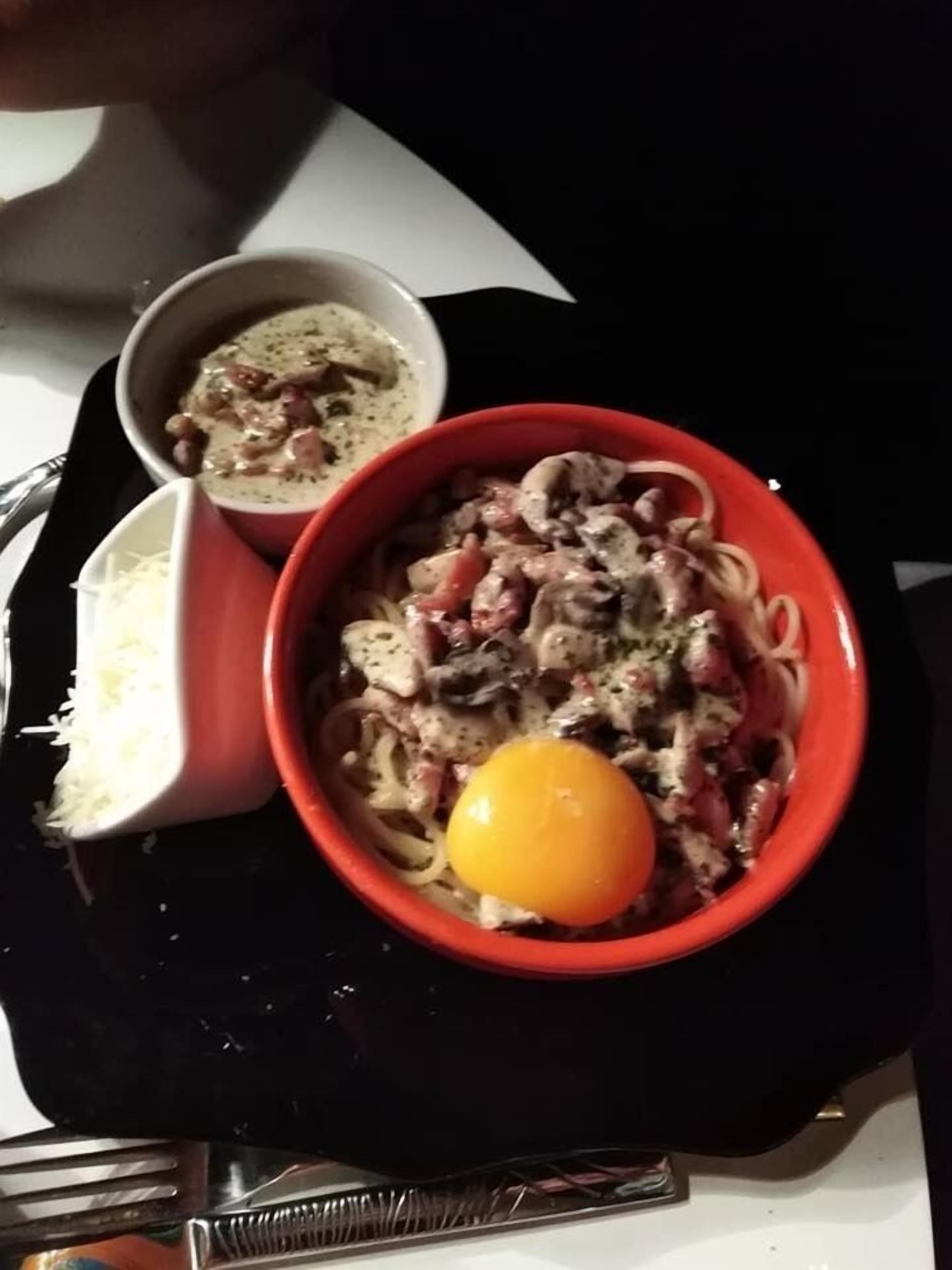 Annoksessa on pastaa ja paistettua kananmunaa, kulho keittoa sekä pieni määrä raastettua juustoa mustalla tarjottimella.