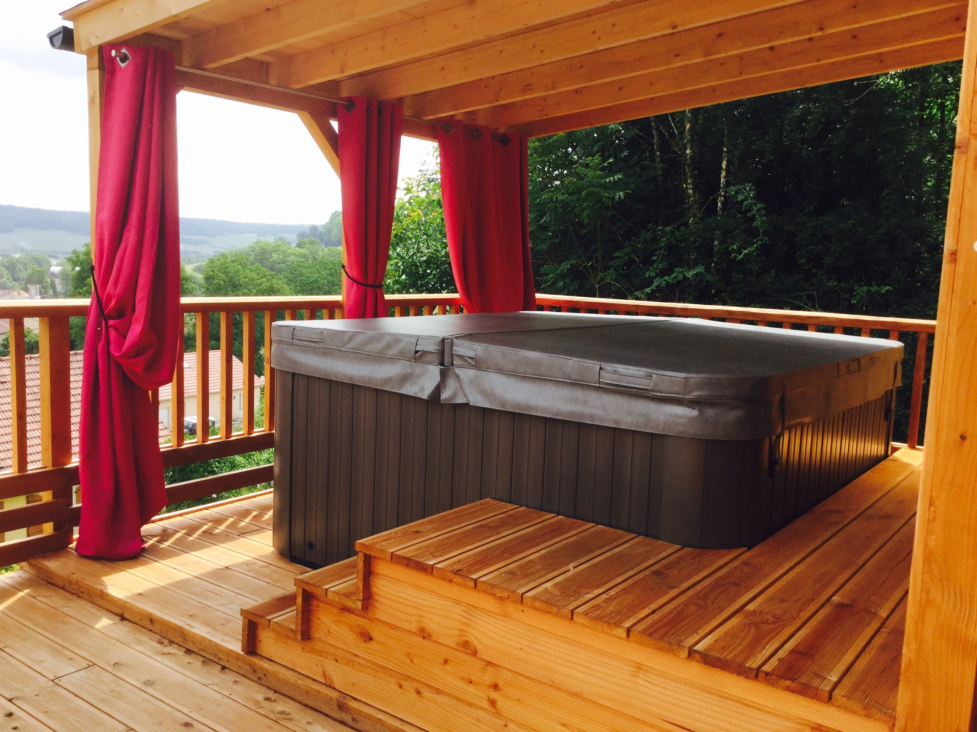 A hot tub on a wooden deck with a view of a forest and hills.
