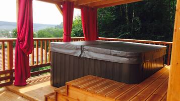 A hot tub on a wooden deck with a view of a forest and hills.