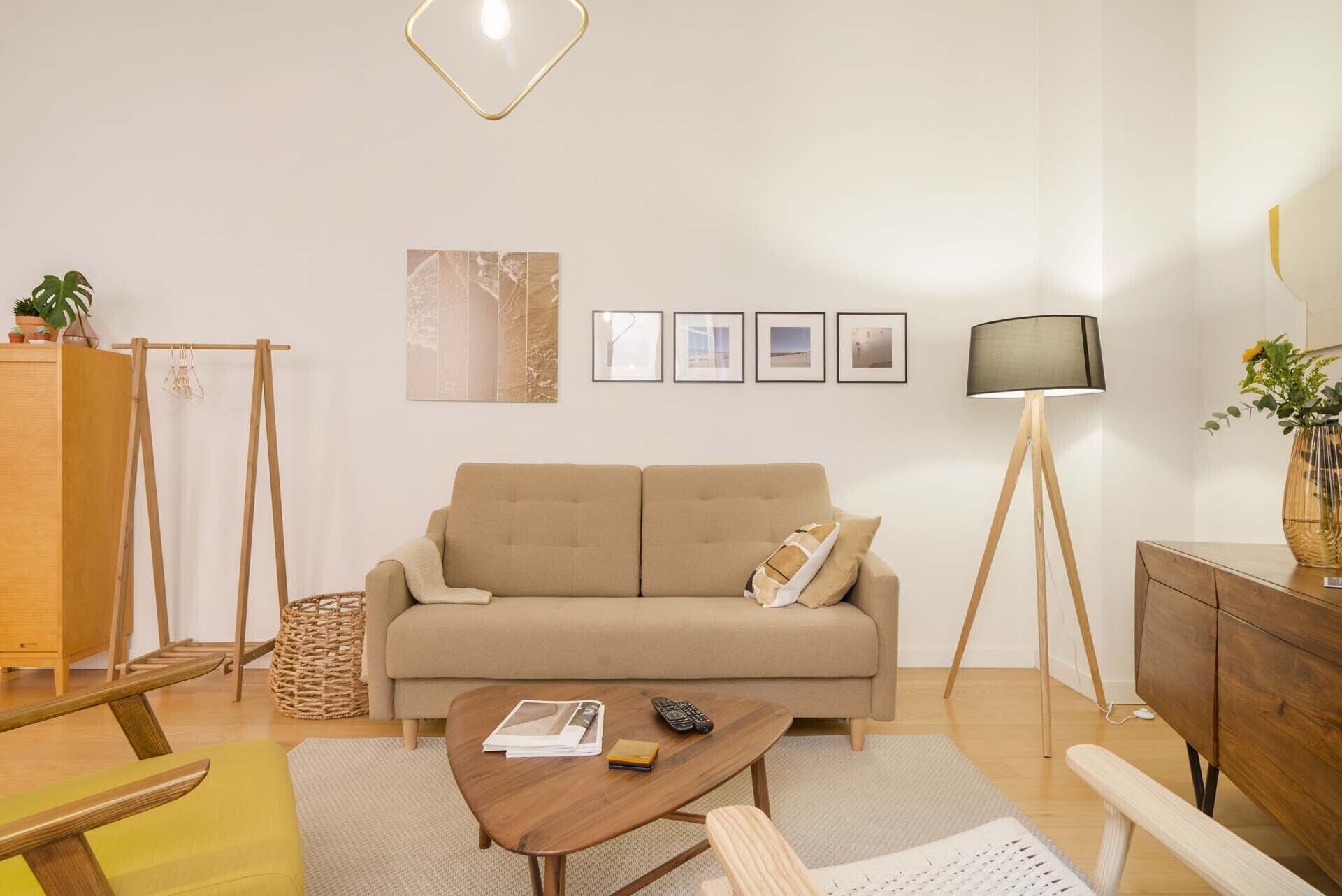 Un salon moderne avec un canapé beige, une table basse en bois, un lampadaire et une petite table d’appoint sur laquelle est posé un vase.