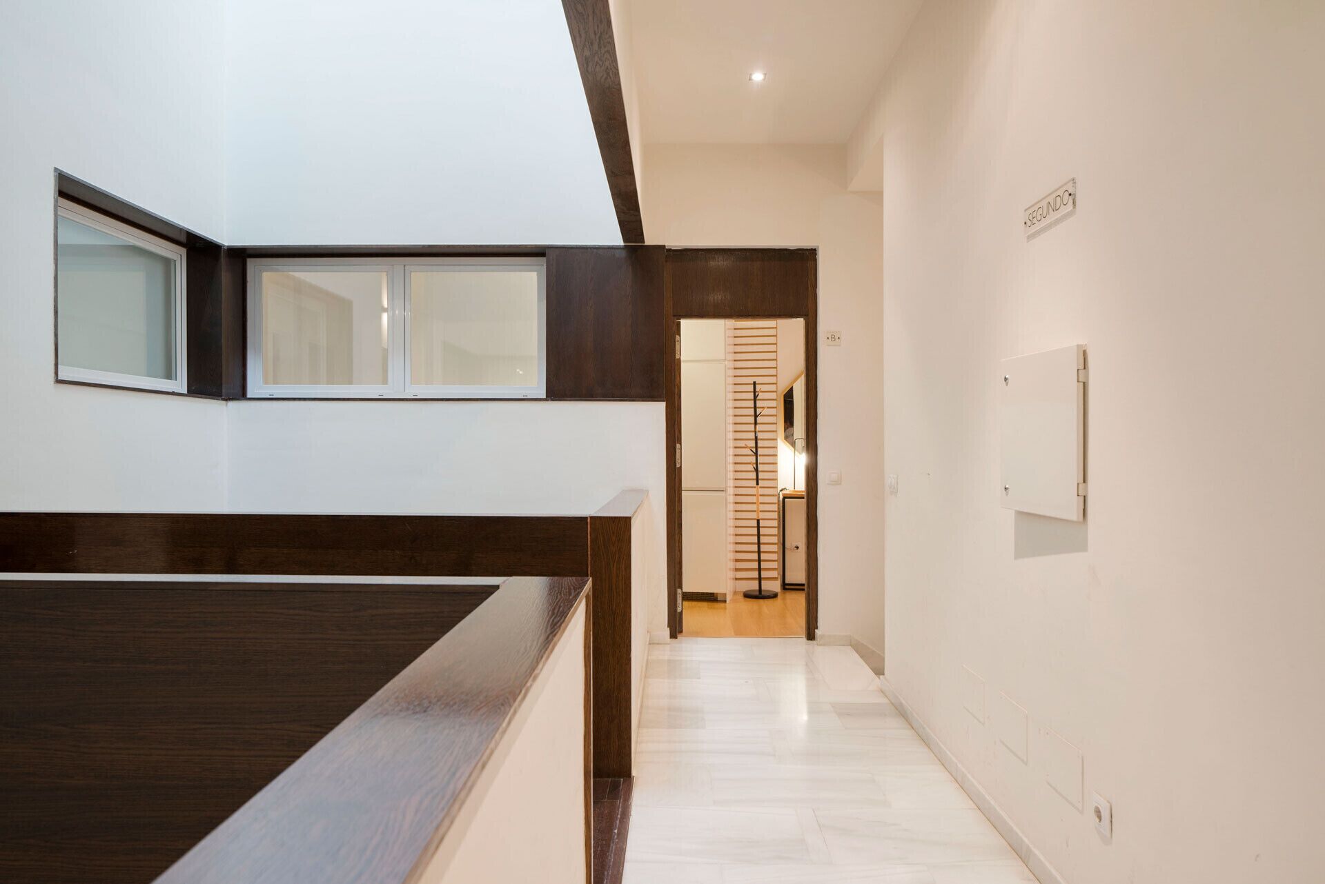 Een moderne hotelgang met een houten receptiebalie, een deur met een spiegeldeur en een bordje dat de tweede verdieping aangeeft.
