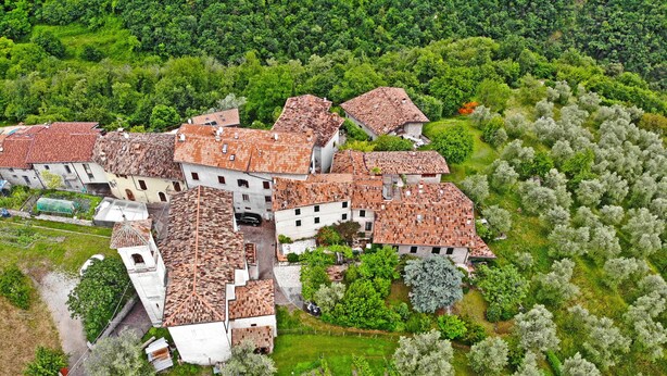 Vista aérea de un pueblo tradicional con edificios de tejas de arcilla, rodeado de exuberante vegetación y viñedos.