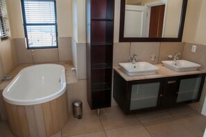 A modern bathroom with a freestanding bathtub, two sinks, a large mirror, and a window with blinds. - 4 Spinnaker (Knysna)