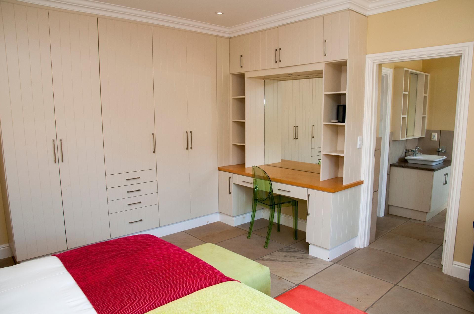Une chambre à coucher avec un lit, un bureau et une chaise. On y trouve une armoire avec plusieurs compartiments, et une salle de bain visible à travers une porte ouverte.