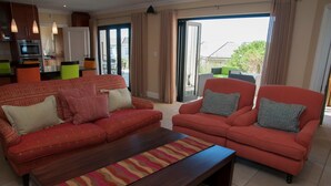 A living room with a red sofa set, a wooden coffee table, and a view through a glass door to the outside. - 4 Spinnaker (Knysna)