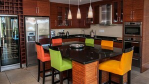 A modern kitchen with wooden cabinets, stainless steel appliances, and a central island with colorful chairs. - 4 Spinnaker (Knysna)