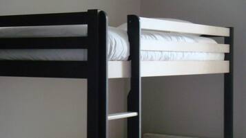 A bunk bed with white bedding and a black frame in a room with plain walls and a radiator.