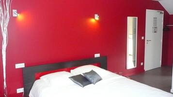 Una habitación con una pared roja, una cama blanca con dos almohadas y una puerta con un espejo.