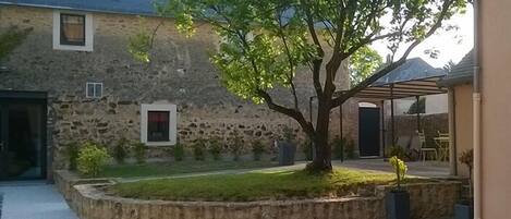 A stone building with a covered patio and a tree in the yard.