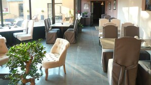Een ruime eetruimte binnen, met hoge plafonds en grote ramen, voorzien van modern meubilair en een centrale tafel met stoelen.