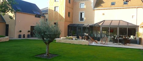 A courtyard with a small tree, a glass-enclosed outdoor seating area, and a building with a sloped roof.