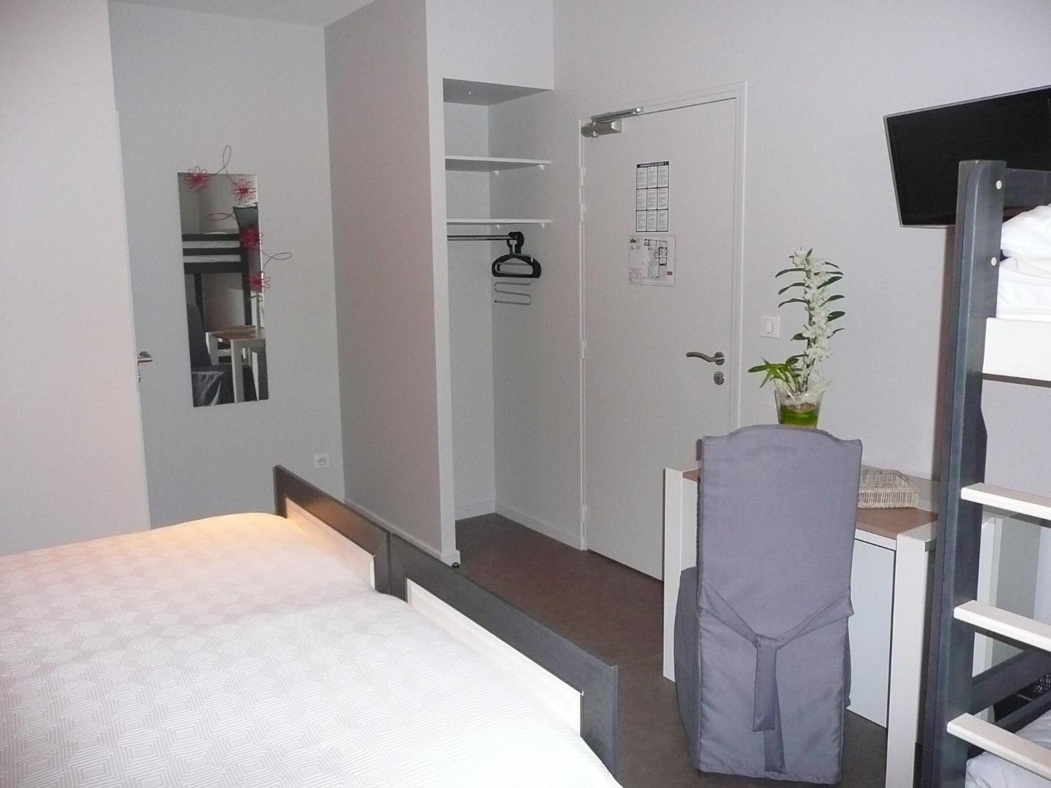 Een slaapkamer met een bed, een bureau, een stoel, een kledingkast en een spiegel.