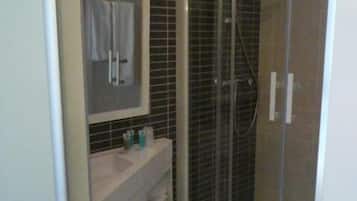 Un baño con ducha envuelta en vidrio, un lavamanos blanco y un espejo sobre él.