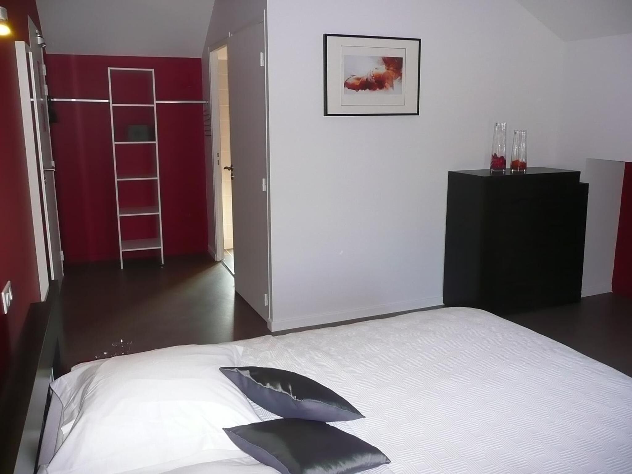 Una habitación de hotel con cama, armario, escritorio y un cuadro en la pared.