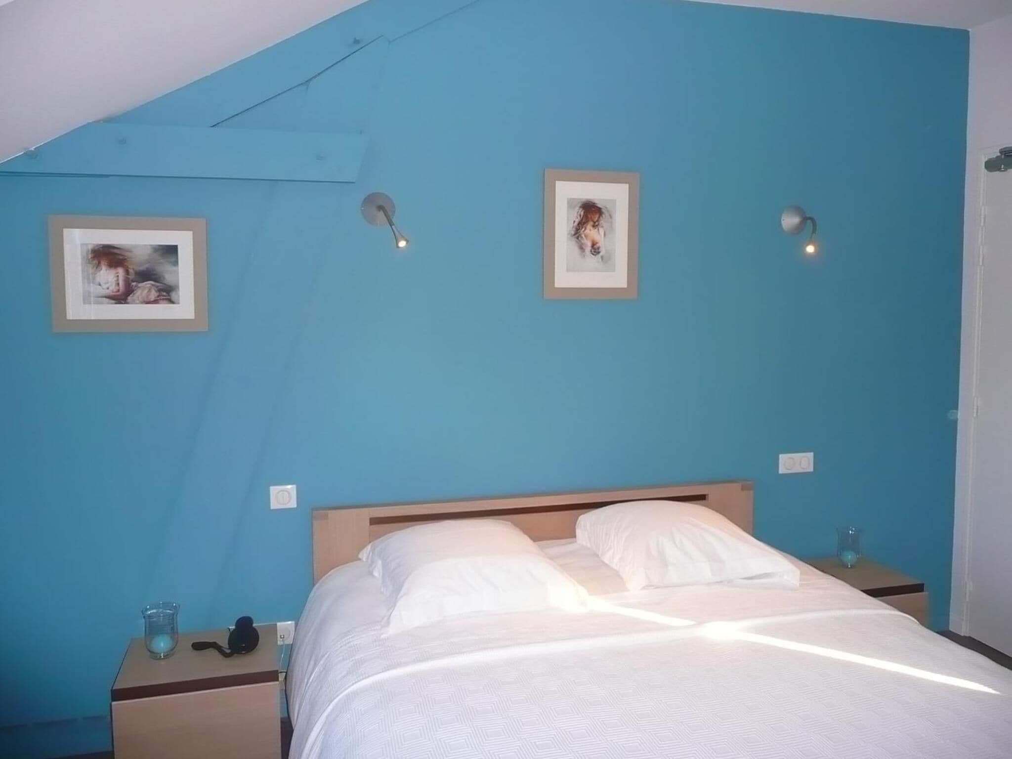 A bedroom with a blue wall, a wooden bed frame, two bedside tables, and two framed pictures on the wall.