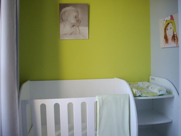 A baby crib with a white frame and a green towel. - Hôtel Le Saint Martin (Sable-sur-Sarthe)