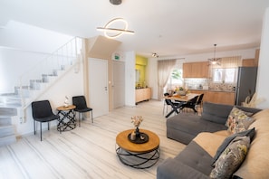 A modern living room with a staircase, a dining area, and a kitchen.