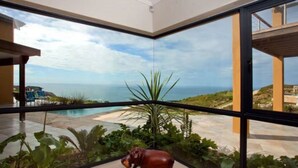 Une chambre d’hôtel moderne avec de grandes fenêtres en verre donnant sur une piscine et la mer.