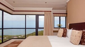 Une chambre avec un grand lit, une vue sur la mer et une fenêtre avec des rideaux.
