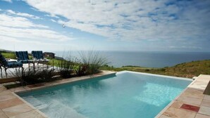 Une piscine rectangulaire offrant une vue dégagée sur l’océan en arrière-plan.