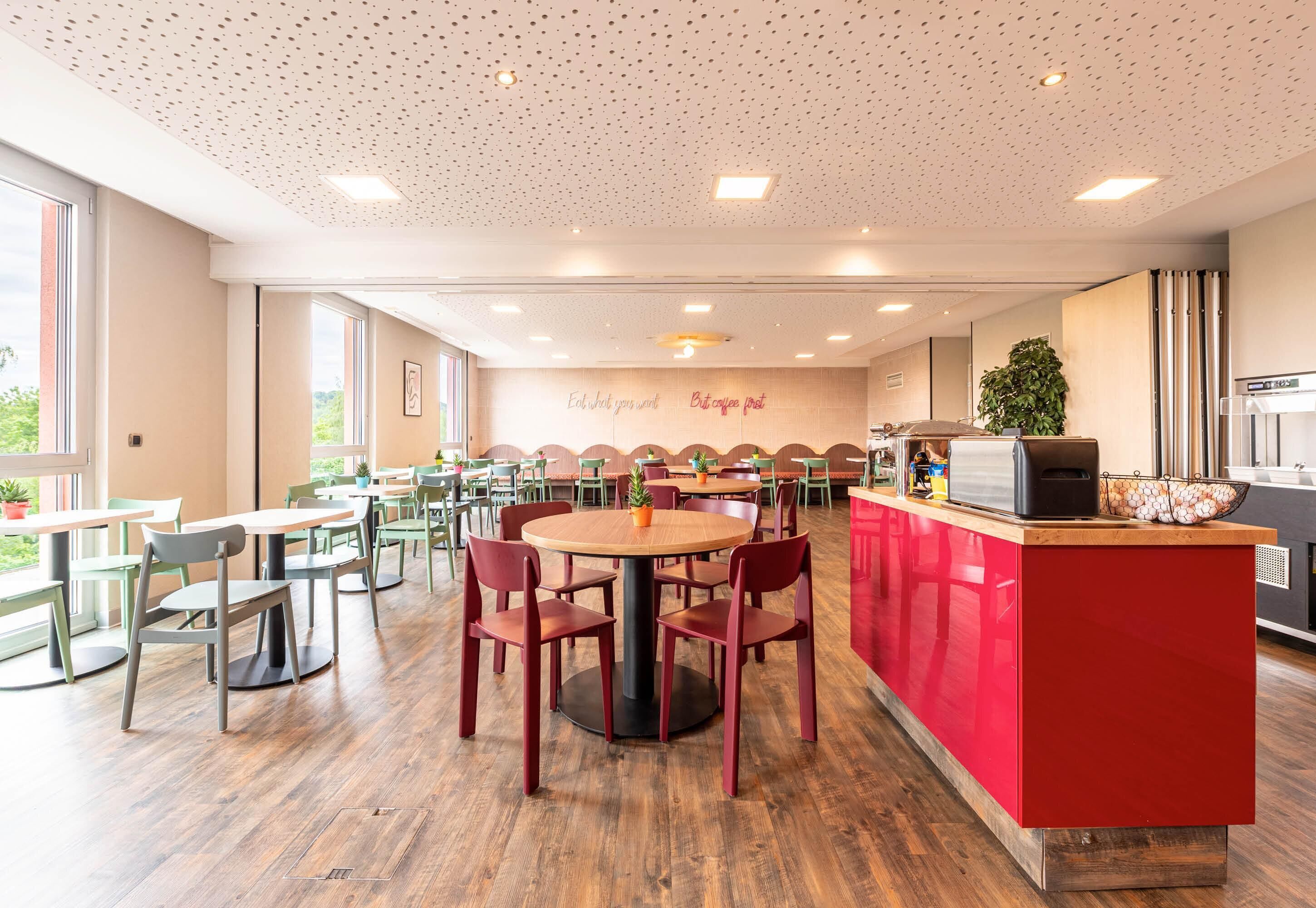 Un espace repas moderne avec des tables et des chaises rondes, un comptoir rouge et un mur orné de citations inspirantes.