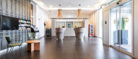 A modern lobby with a flat-screen TV, seating area, and a reception desk.