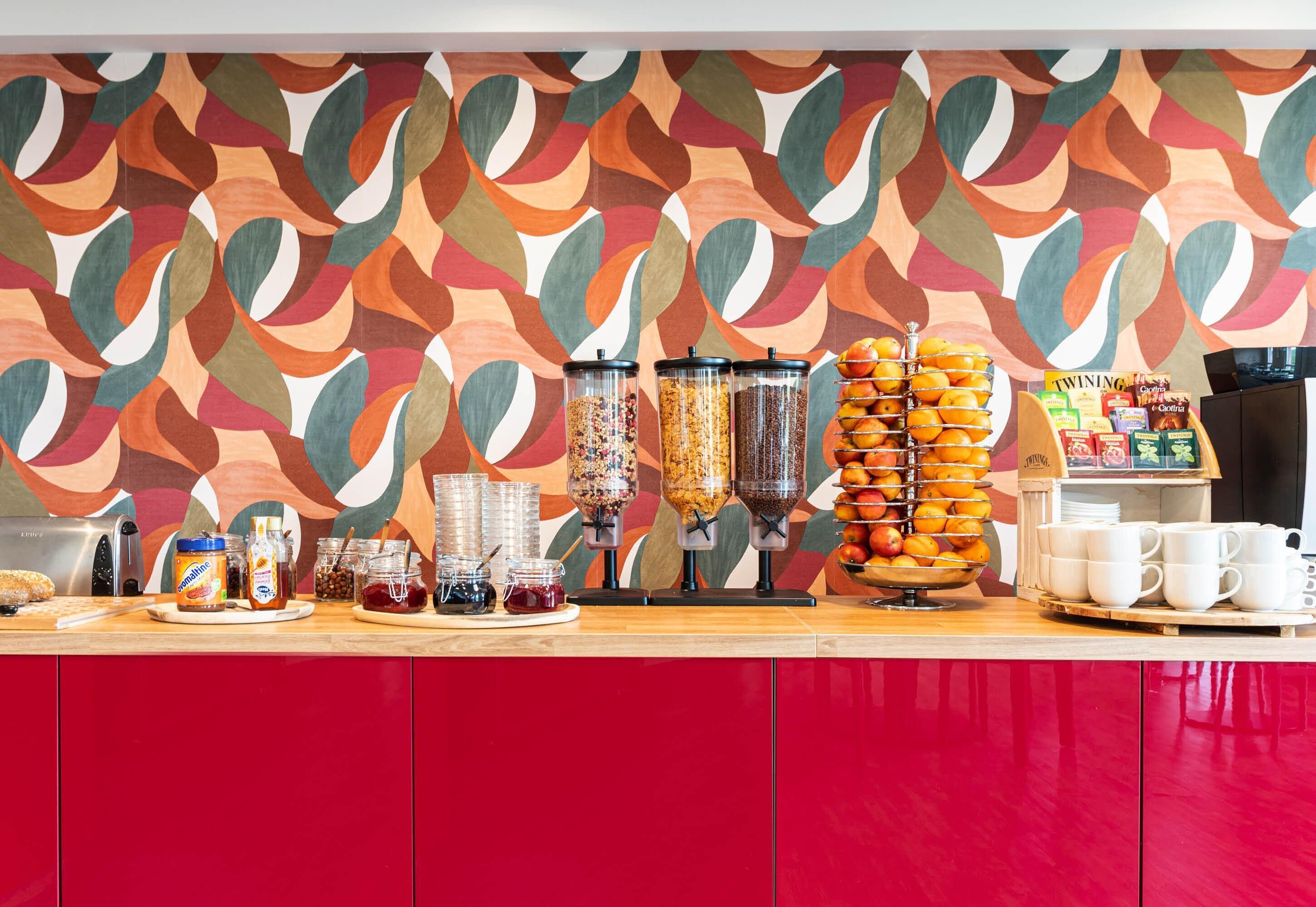 A breakfast bar with various food items, a coffee machine, and a colorful abstract wall.