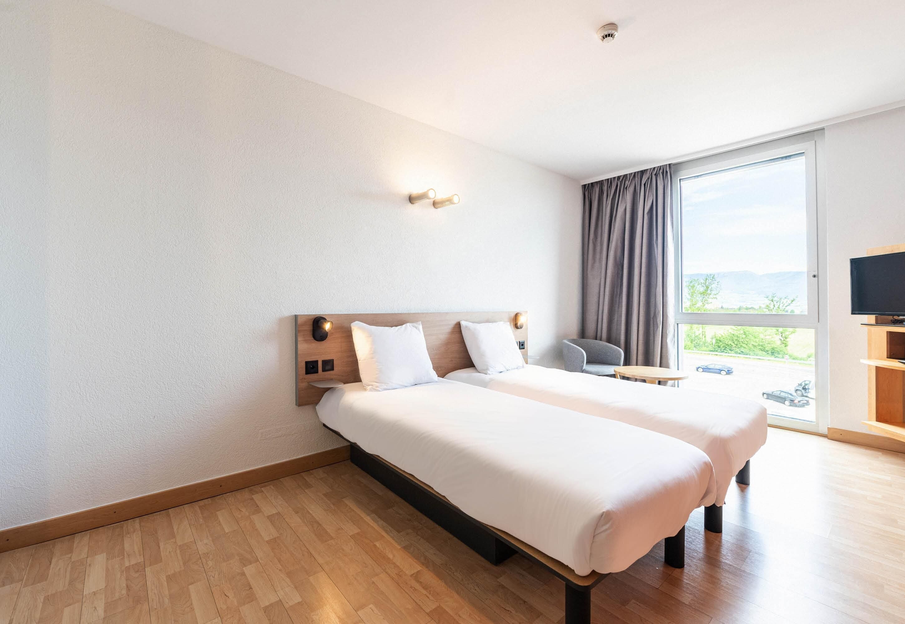 A hotel room with two beds, a TV, a chair, and a large window with a view.