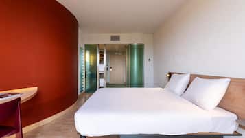 A hotel room with a bed, a desk, and a chair. There is a door leading to another room.