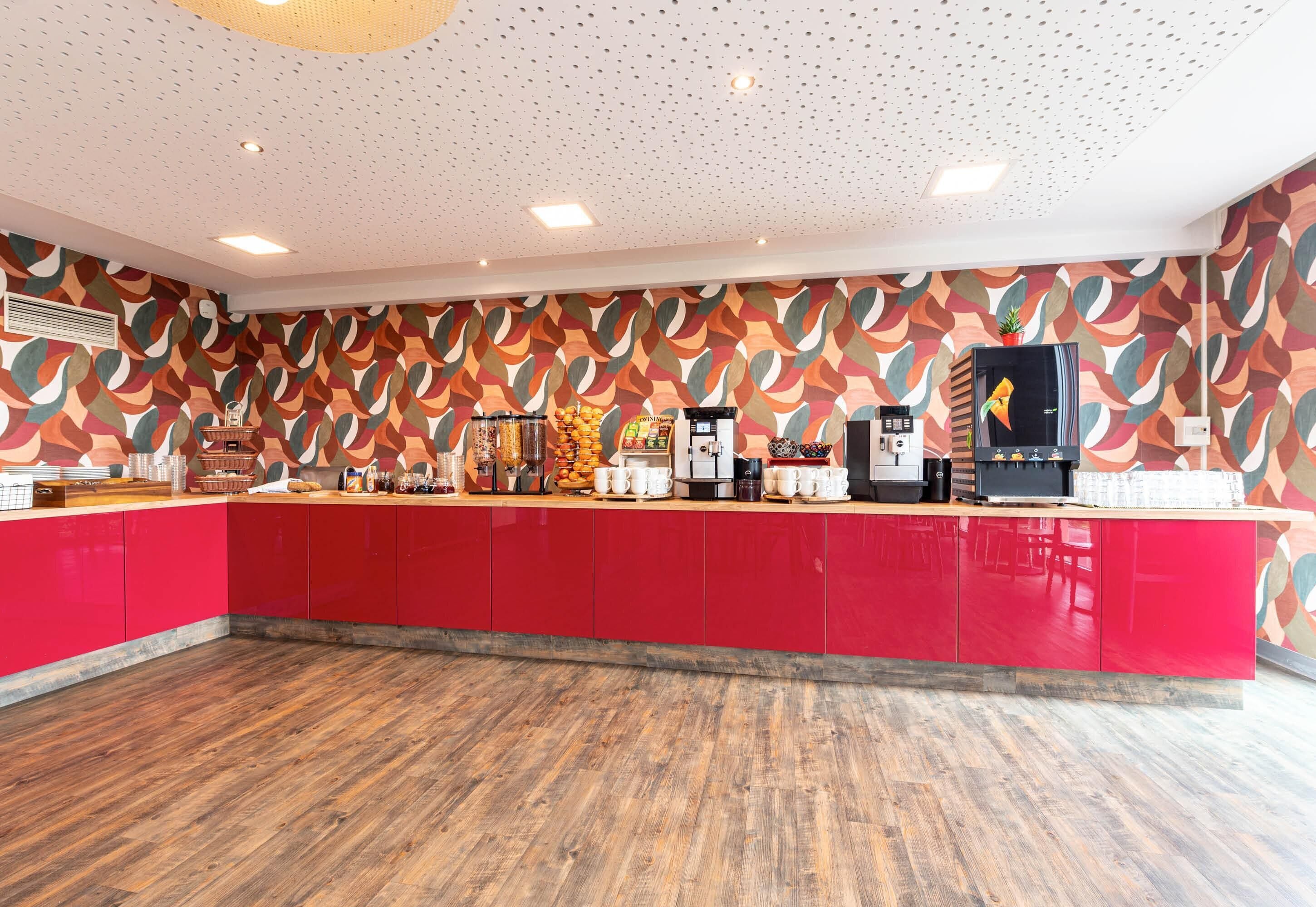 A modern kitchen with red cabinets, a wooden floor, and a patterned wall.