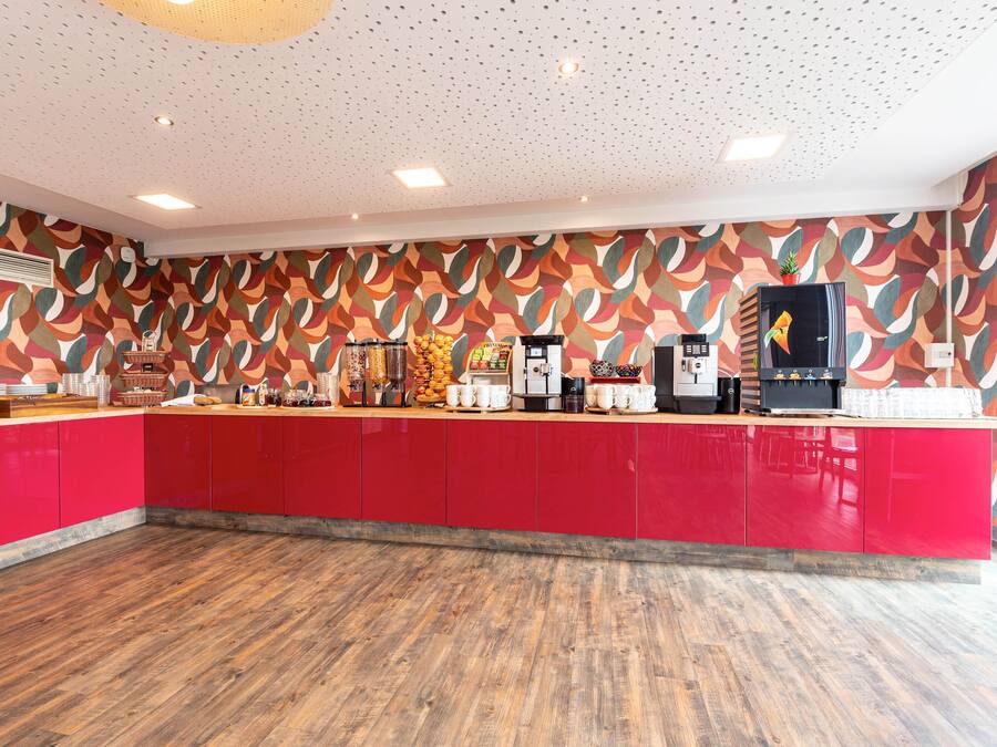 A modern kitchen with red cabinets, a wooden floor, and a patterned wall.