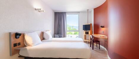 Quarto de hotel com cama, escrivaninha, cadeira, televisão e janela com vista.