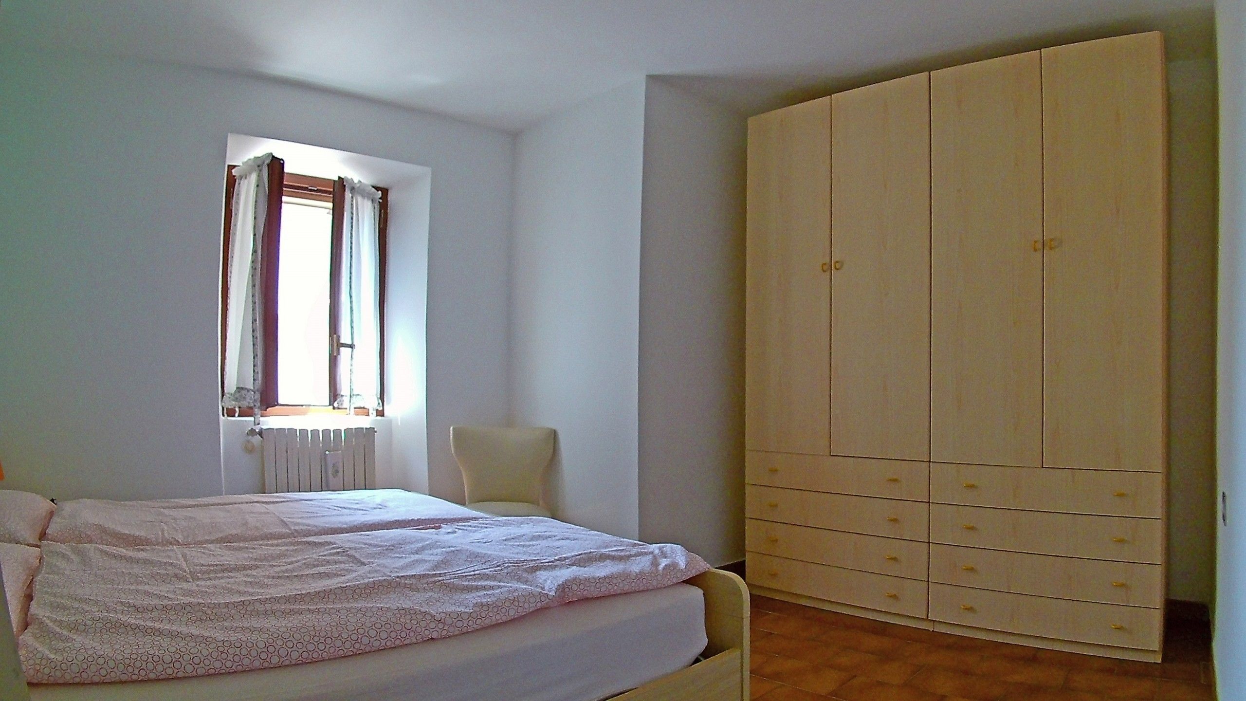 A bedroom with a bed, a window with curtains, and a wardrobe.
