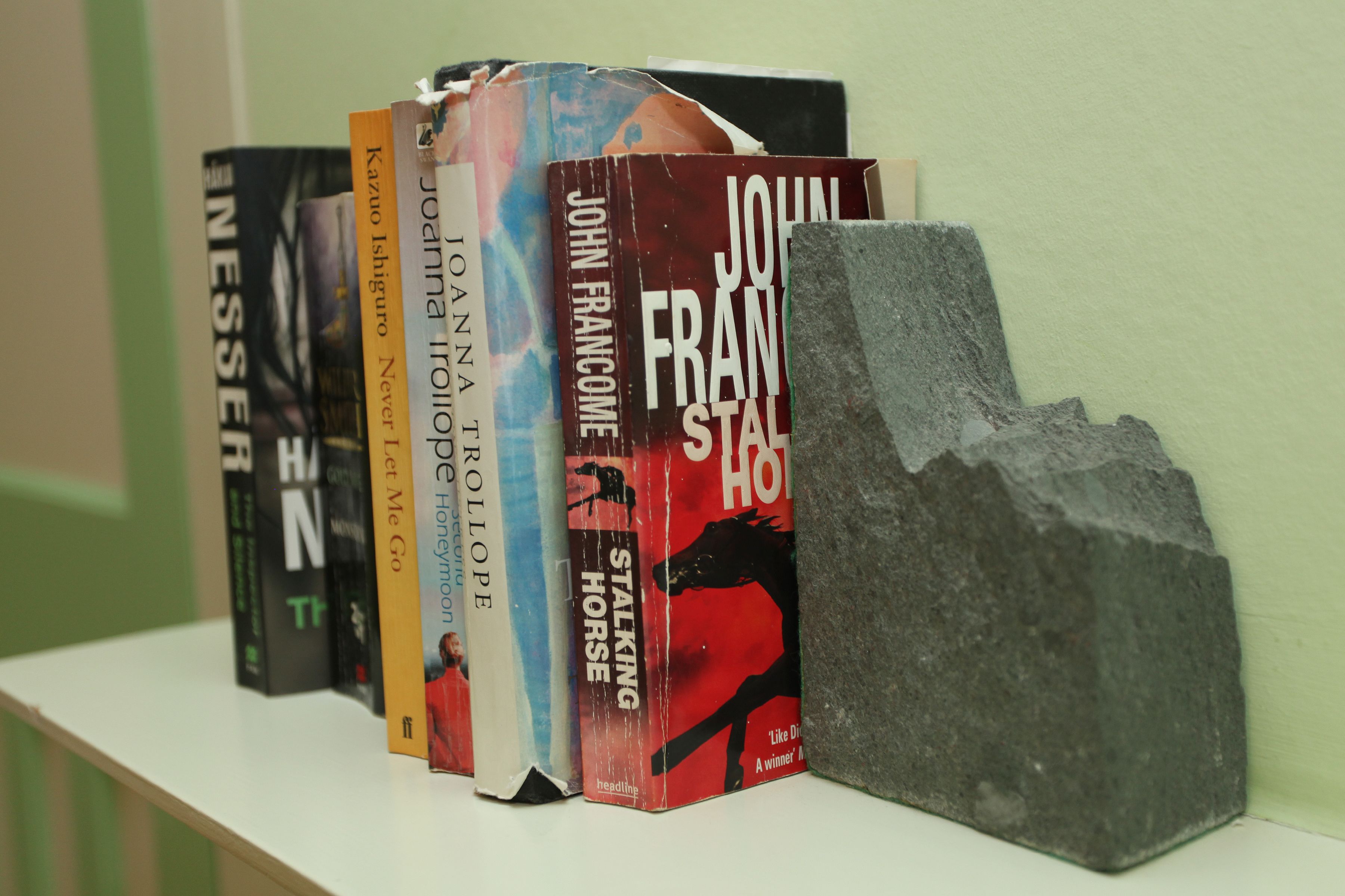 A row of books on a shelf with a stone block beside them.