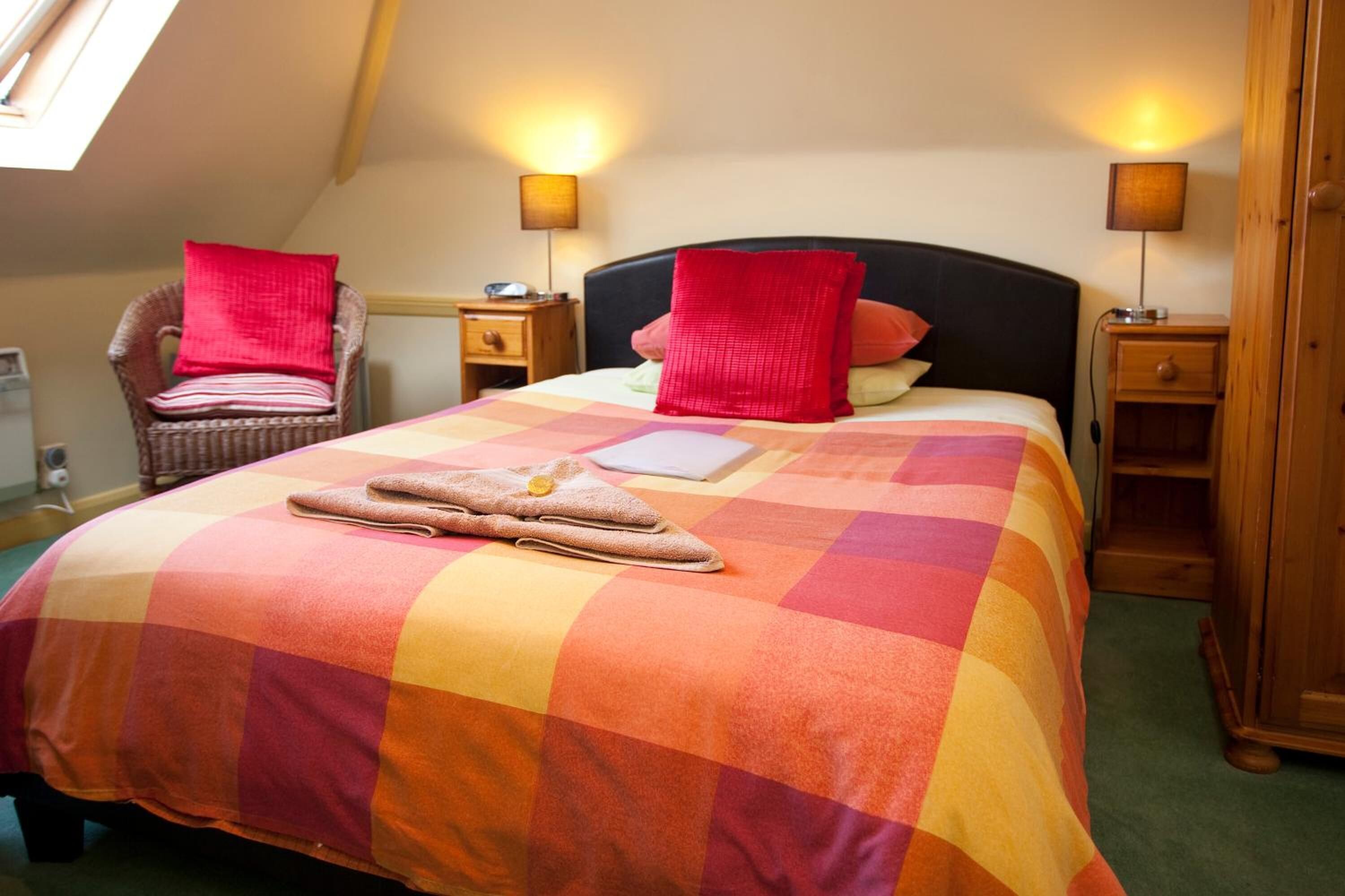 A bedroom with a large bed, two nightstands, a chair, and a wooden wardrobe.