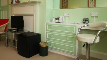 A room with a television, a small black refrigerator, a green dresser with drawers, a white chair, and a trash can.