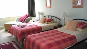 Une chambre avec deux lits, chacun recouvert d’une couverture à carreaux rouges et blancs, une table de chevet avec une lampe et une fenêtre avec des rideaux.